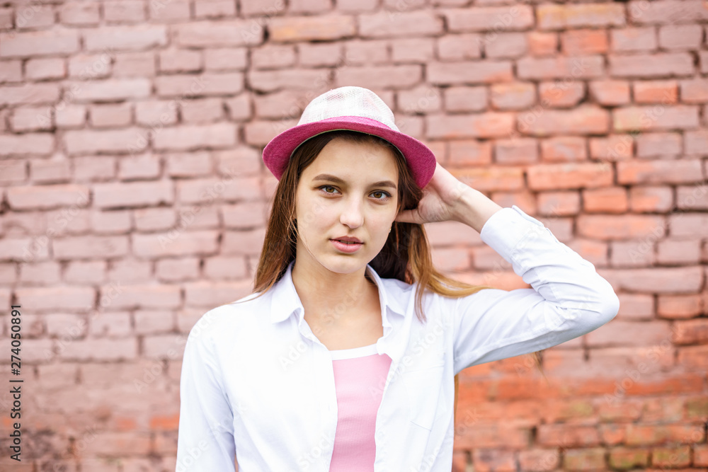close up portrait of beautiful stylish kid girl in hat near pink brick wall as background close up portrait of beautiful stylish kid girl in hat near pink brick wall as background