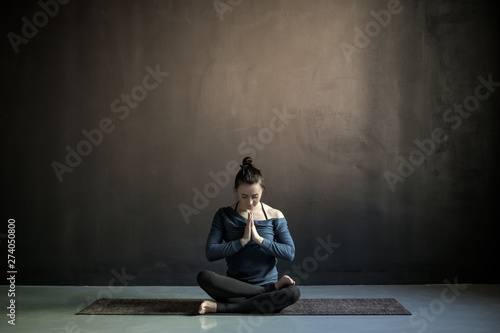 Young woman preparing to practice yoga, sitting on meditation session. Full length. Studio black wall with copyspace