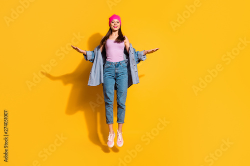 Full length body size photo beautiful she her lady hands arms raised sides air jump high sportive day off amazing look wear casual jeans denim jacket shoes pink hat isolated yellow bright background