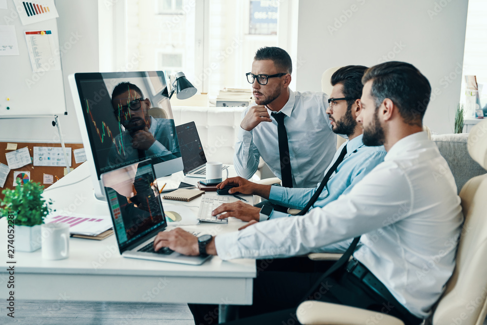 Teamwork. Group of young modern men in formalwear analyzing stock market data while working in the office Teamwork. Group of young modern men in formalwear analyzing stock market data while working in the office