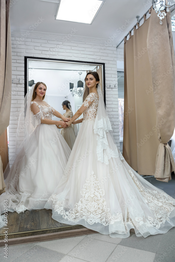 Naklejka premium Two happy women in wedding dresses posing in salon