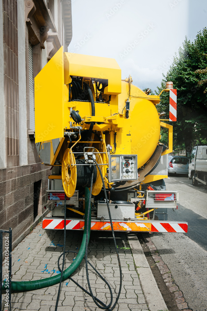 Rear view of powerful professional modern yellow sewage sewerage truck working near a house pumping basement canalisation water