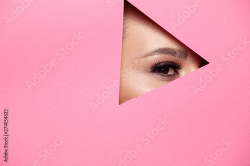A girl with beautiful curry bright beautiful eyes with brown shadows and expressive eyebrows looks into the hole of colored paper.Fashion, beauty, make-up, cosmetics, make-up artist, beauty salon,busi © pokryvka