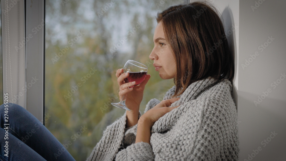 Young woman with glass of drink in coverlet near window Young woman with glass of drink in coverlet near window