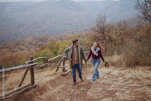 Full length of smiling multicultural couple dressed casual taking a walk in nature and holding hands. Woman holding bouquet. Autumn season.