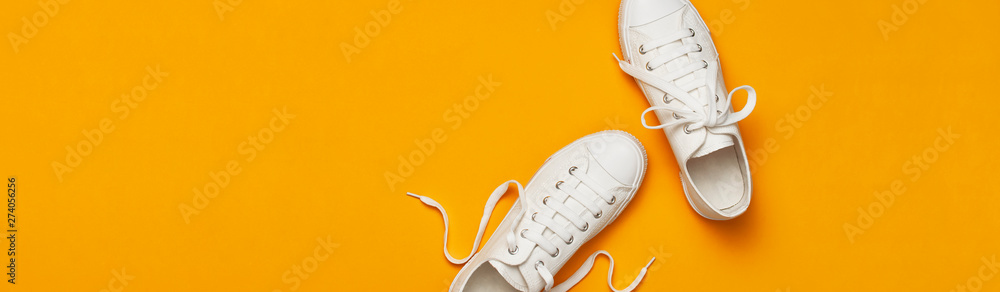 White female fashion sneakers on yellow orange background. Flat lay top view copy space. Women's shoes. Stylish white sneakers. Fashion blog or magazine concept. Minimalistic shoe background, sport - obrazy, fototapety, plakaty 