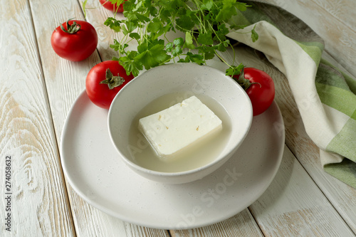 Принти на полотні a bowl of feta cheese in brine and tomatoes on a light wooden table