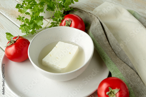 Photography feta cheese in brine in a ceramic bowl, fresh tomatoes and parsley on a light wo