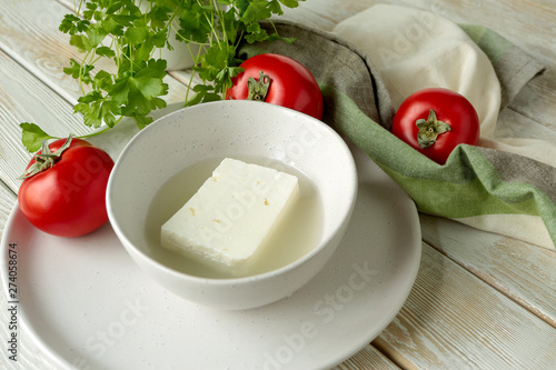 Foto feta cheese in brine in a ceramic bowl, fresh tomatoes and parsley on a light wo