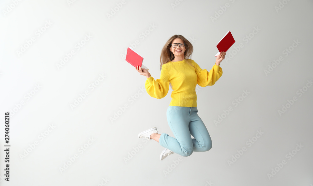 Jumping young woman with books on light background Jumping young woman with books on light background