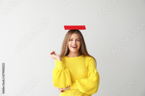 Happy young woman with books on light background