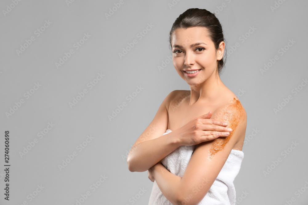 Fototapeta premium Beautiful young woman applying body scrub against grey background
