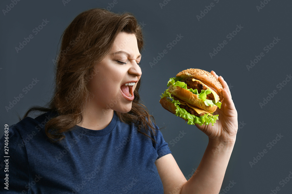 Plus size woman with tasty burger on grey background. Concept of body positive Plus size woman with tasty burger on grey background. Concept of body positive