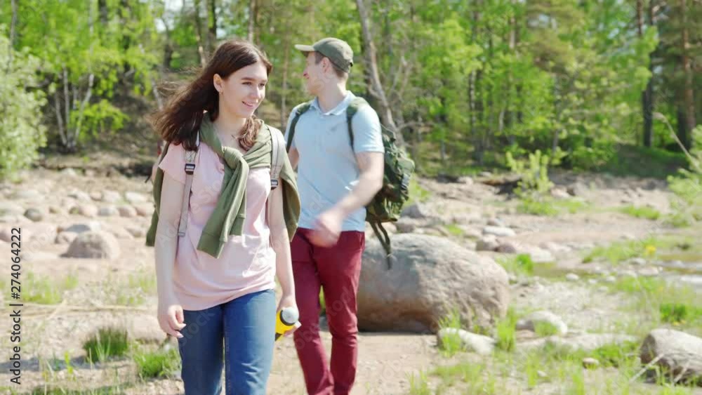 Tilt up of group of four cheerful young hikers, men and women, with backpacks walking on stones and talking during adventure on summer day Tilt up of group of four cheerful young hikers, men and women, with backpacks walking on stones and talking during adventure on summer day