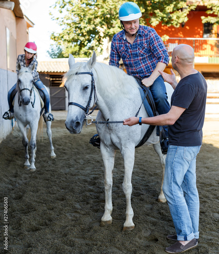 Mature couple with trainer riding horse at farm outdoor © JackF