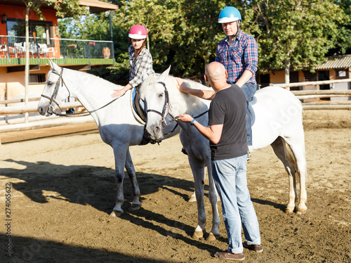 Woman and man with trainer riding horse at farm at summer day