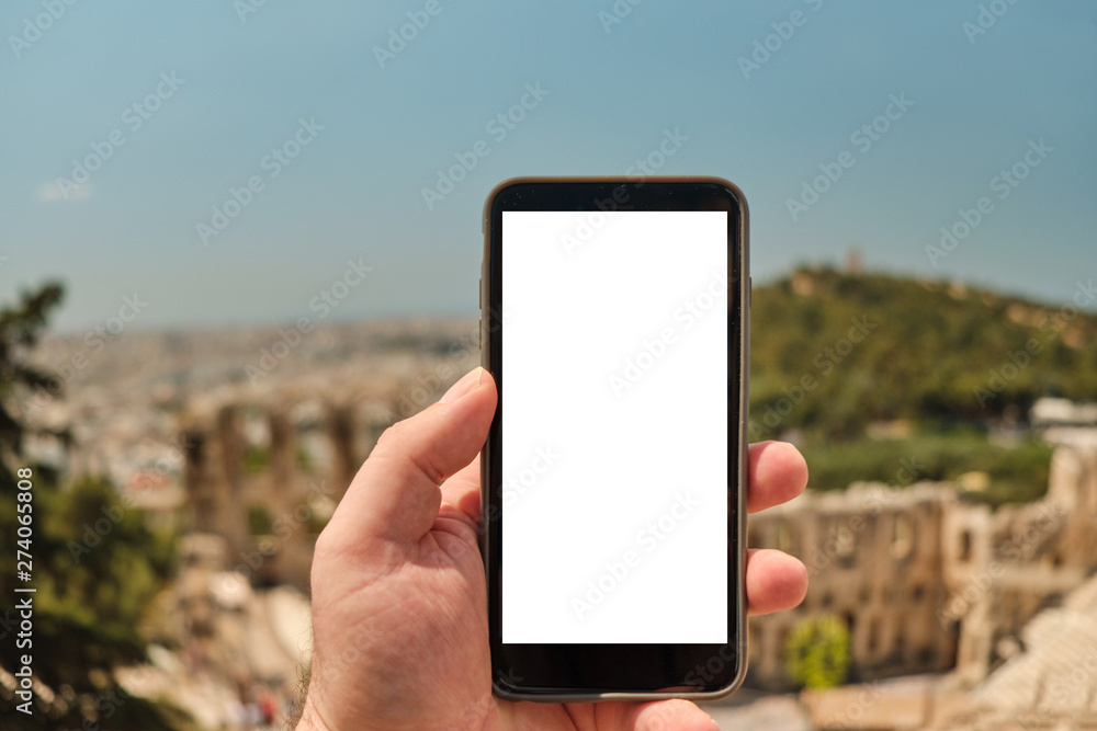 hand of man holding smart phone in front of the ancient area o the Athens Greece, theater under acropolis - Odeon of Herodes Atticus near Acropolis in a sunny day in the capital Greece - Athens.