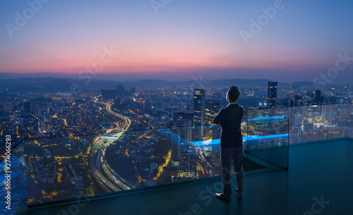 Businessman standing on open roof top balcony watching city night view . Business ambition and vision concept . photo