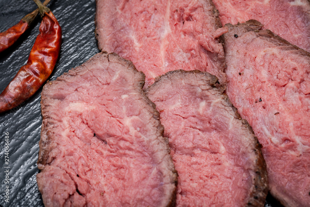 Sliced Grass Fed Juicy Corn Roast Beef garnished with dried Red Chile De Arbol Pepper on black natural stone background. Sliced Grass Fed Juicy Corn Roast Beef garnished with dried Red Chile De Arbol Pepper on black natural stone background.