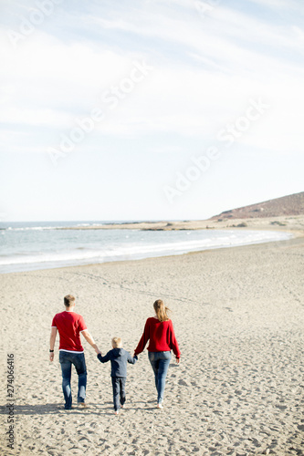 Small child with parents walks along the beach against backdrop of hills and small mountain. The relationship between friends, adolescence. Travel to other countries. Life on the ocean. View backside.