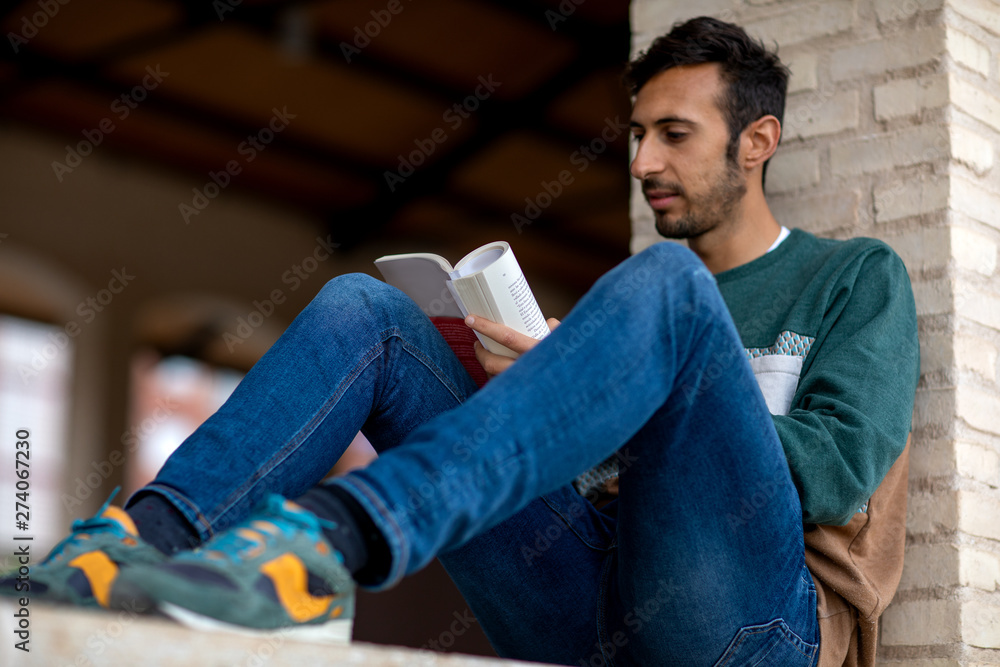 Young Bearded Man Reading A Book Sitting In A Park During The Morning Young Bearded Man Reading A Book Sitting In A Park During The Morning