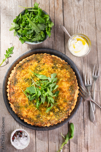 Quiche with arugula, onion, spinach, mozzarella, feta and sauce on rustic background, top view. Homemade, traditional french quiche pie.