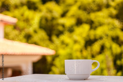 a small white cup of coffee on a blurry natural background