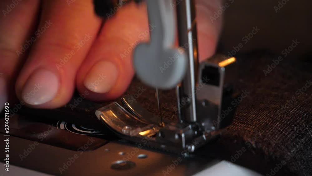 Sewing Machine Needle in Motion. Close-up of sewing machine needle rapidly moves up and down. The tailor sews black fabric on the sewing workshop. The process of sewing fabric. Sewing Machine Needle in Motion. Close-up of sewing machine needle rapidly moves up and down. The tailor sews black fabric on the sewing workshop. The process of sewing fabric.