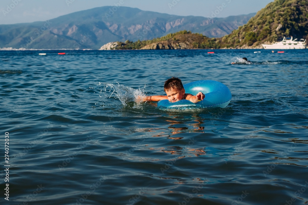 five-year-old boy in a blue lifebuoy learns to swim in the sea, Turkey