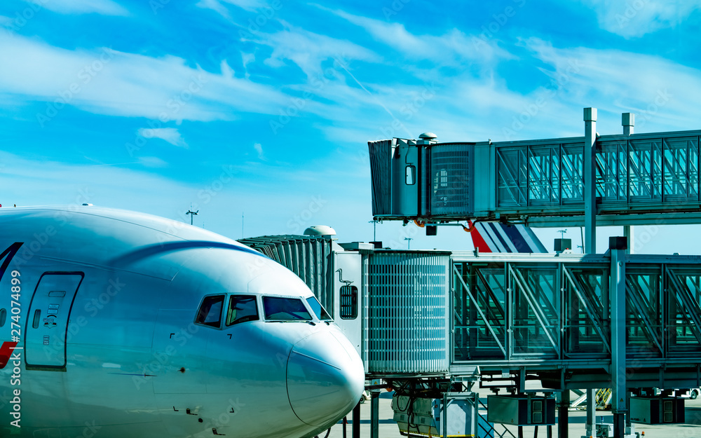Commercial airline parked at jet bridge for passenger take off at the airport. Aircraft passenger boarding bridge docked with blue sky and white clouds. Departure flight of international airline. Commercial airline parked at jet bridge for passenger take off at the airport. Aircraft passenger boarding bridge docked with blue sky and white clouds. Departure flight of international airline.