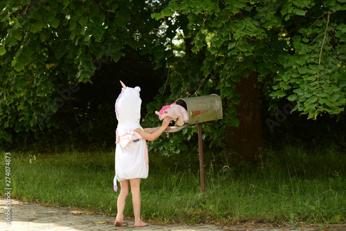 Eine welt voller Einhörner. Kleines verkleidetes Mädchen holt Plüschtier aus Briefkasten photo