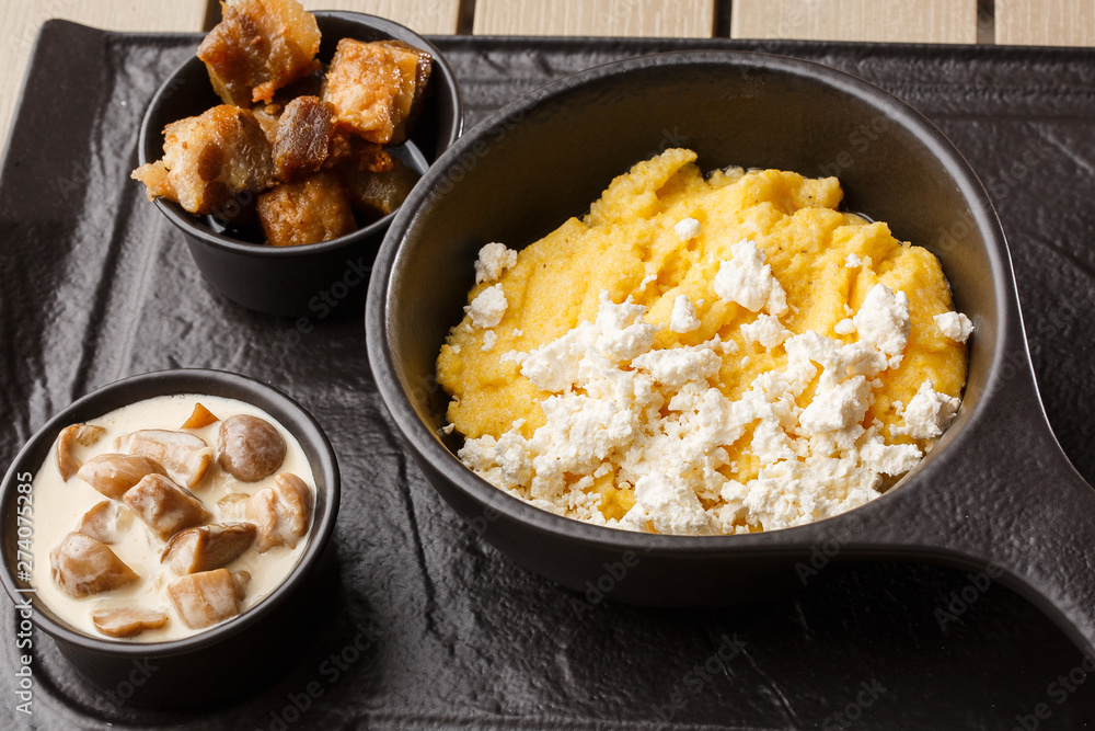 Typical Ukrainian dish polenta - Banosh with cheese and lard. Ukrainian cuisine. maize porridge with bacon, cracklings and cheese Corn porridge in plate on wooden background. Typical Ukrainian dish polenta - Banosh with cheese and lard. Ukrainian cuisine. maize porridge with bacon, cracklings and cheese Corn porridge in plate on wooden background.
