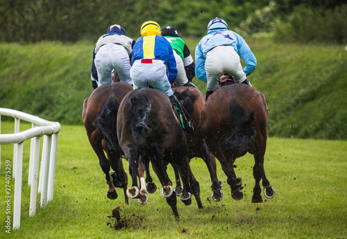 Jockeys and race horses racing down the track in the rain, view from behind