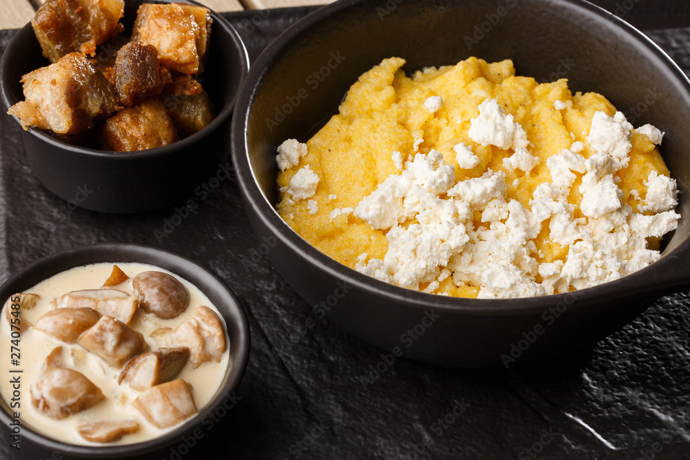Typical Ukrainian dish polenta - Banosh with cheese and lard. Ukrainian cuisine. maize porridge with bacon, cracklings and cheese Corn porridge in plate on wooden background. Typical Ukrainian dish polenta - Banosh with cheese and lard. Ukrainian cuisine. maize porridge with bacon, cracklings and cheese Corn porridge in plate on wooden background.