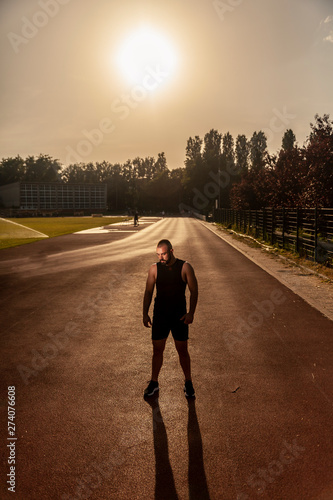 One young muscular athlete man, posing on sports field, on a hot Summer day, outdoors. Sun in sky.