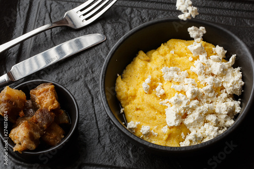 Typical Ukrainian dish polenta - Banosh with cheese and lard. Ukrainian cuisine. maize porridge with bacon, cracklings and cheese Corn porridge in plate on wooden background.