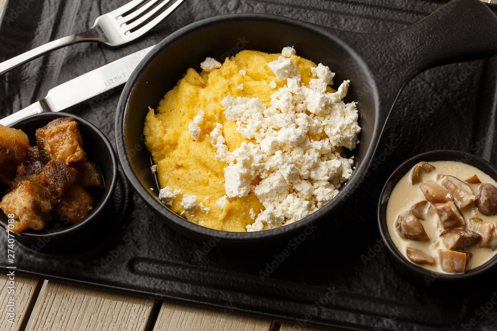 Typical Ukrainian dish polenta - Banosh with cheese and lard. Ukrainian cuisine. maize porridge with bacon, cracklings and cheese Corn porridge in plate on wooden background. Typical Ukrainian dish polenta - Banosh with cheese and lard. Ukrainian cuisine. maize porridge with bacon, cracklings and cheese Corn porridge in plate on wooden background.