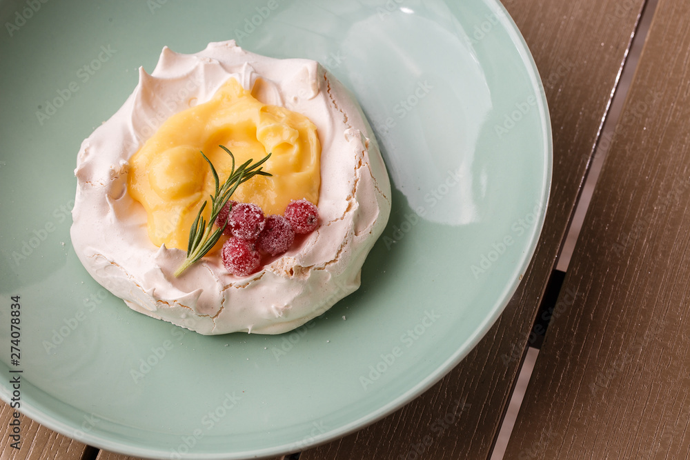 Pavlova mini cake with custard cream and fresh summer berries on green plate on wooden background. Baked meringue cake. Pavlova mini cake with custard cream and fresh summer berries on green plate on wooden background. Baked meringue cake.
