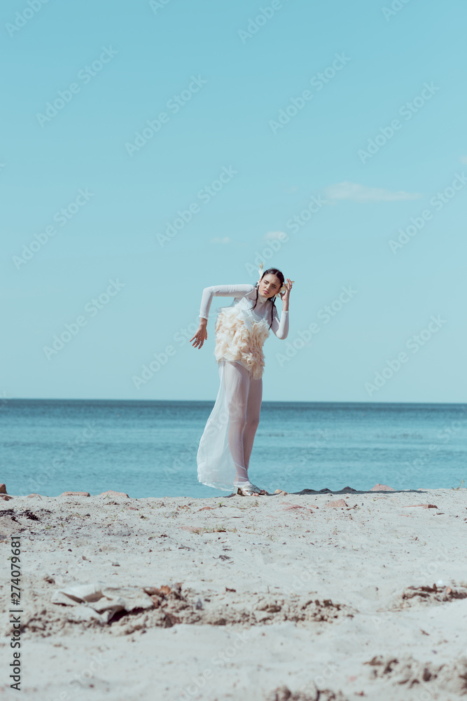 tender woman in white swan costume standing on sandy beach