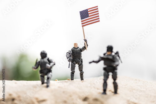 selective focus of toy soldier with weapon holding american flag on sand