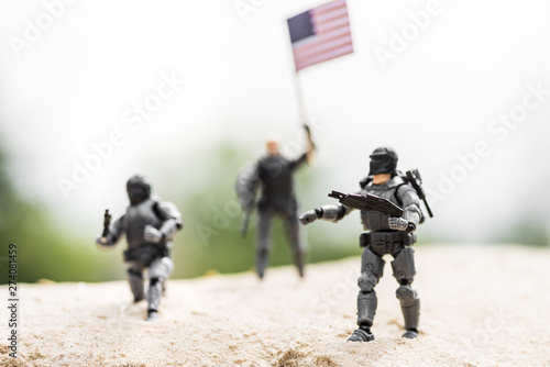 Selective focus of toy soldiers with weapon and American flag on sand