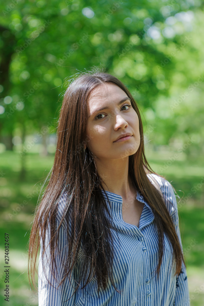 A girl of Asian appearance in a city park. Summer portrait of young Tatar on a background of green foliage A girl of Asian appearance in a city park. Summer portrait of young Tatar on a background of green foliage