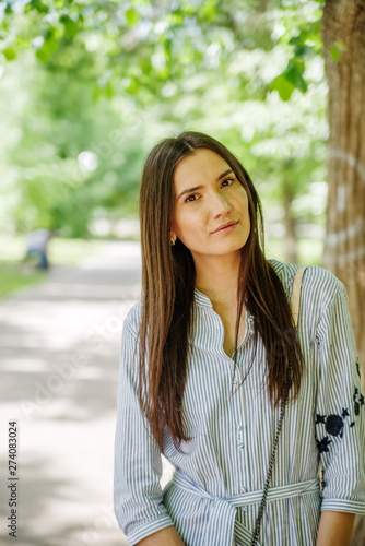 A girl of Asian appearance on a walk in a city park. Summer portrait of young Tatar on a background of green foliage