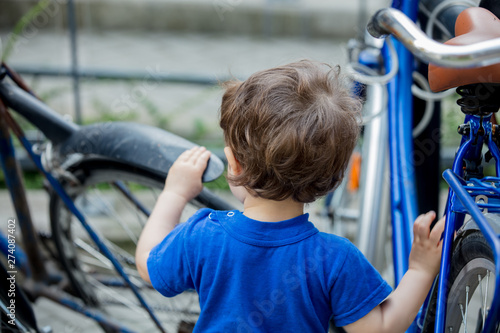 little toddler boy plays enthusiastically with big bikes on a city bike parking