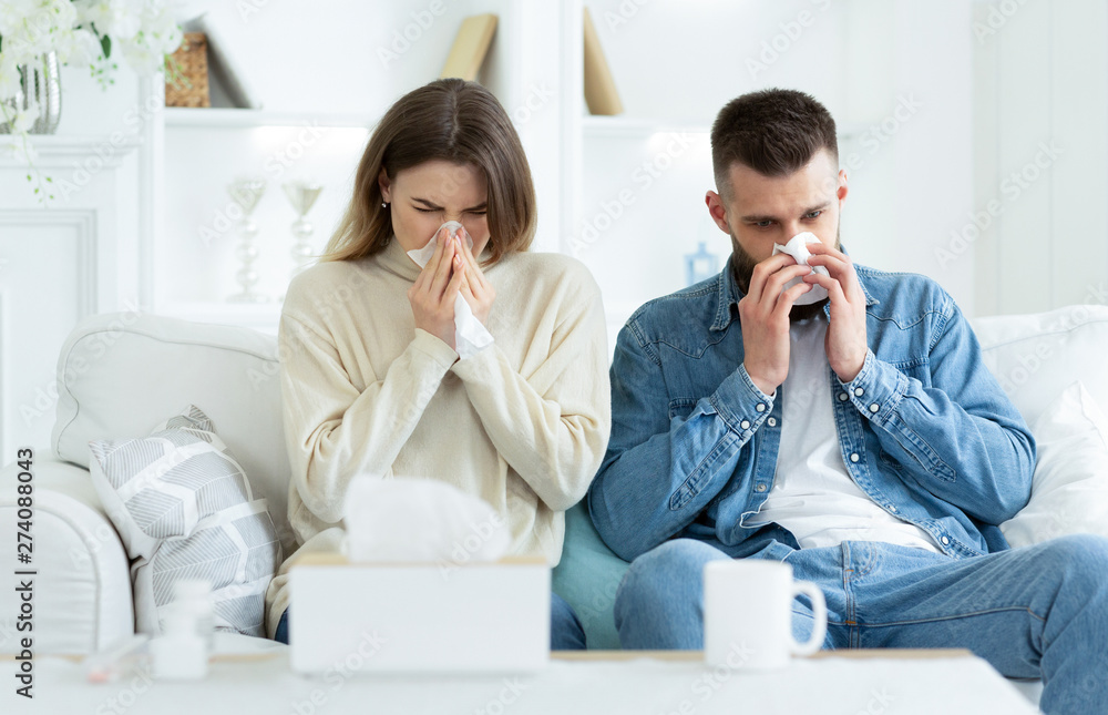 Couple Suffering From Cold, Blowing Noses And Sneezing Couple Suffering From Cold, Blowing Noses And Sneezing
