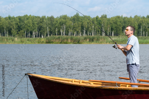 a man in sunglasses on a boat is fishing with the help of spinning in beautiful weather on the lake, active recreation