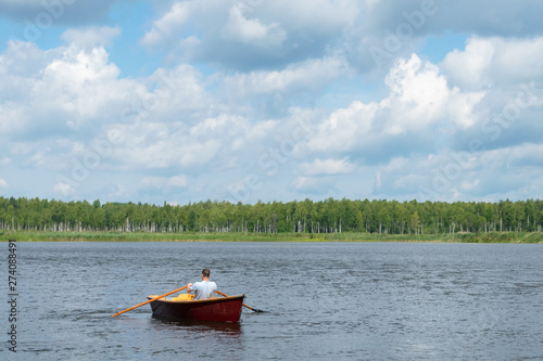 a man is floating in a wooden boat on a lake on a nice sunny day, an active weekend
