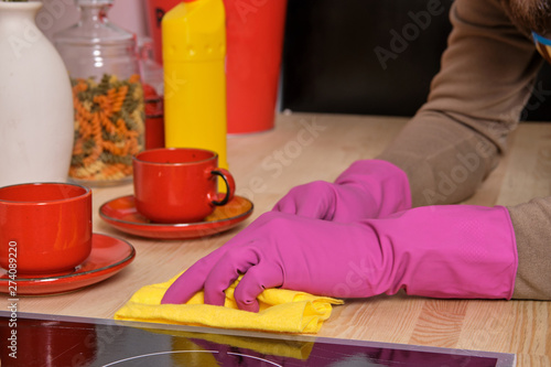 Young handsome bearded man in the kitchen, wearing apron and pink gloves cleans the cooking surface using detergents