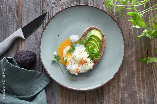 Avocado sandwich with dark bread, sliced avocado and poached egg, flat lay on rustic wood