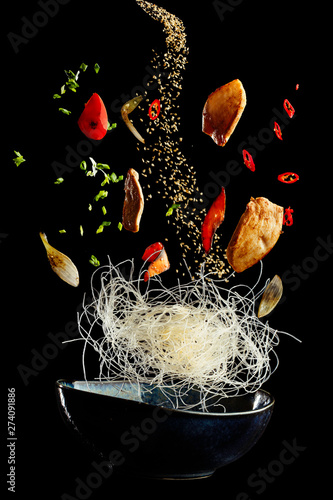 flying wok with chicken and spices. Concept of food preparation in low gravity mode, food levitation. Separated on black background. High resolution image